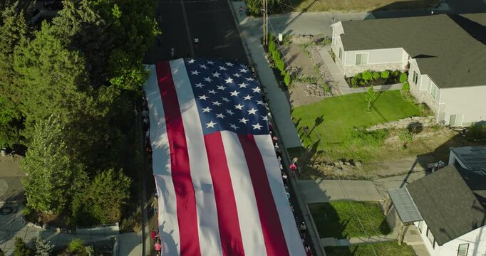 Majestic, large American flag being escorted down neighborhood street - cinematic aerial shot