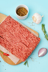 Wooden board of fresh minced meat with spices on blue background