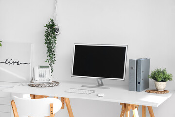 Blank computer monitor with telephone on table in light office