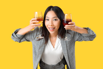 Beautiful Asian businesswoman with glasses of wine on yellow background