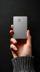 Hand holding blank unbranded modern gray credit card with chip on dark background