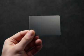 Hand holding blank unbranded modern gray card on dark background