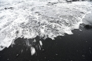 Waves gently wash over the volcanic black sand of Punaluʻu Beach on the Big Island of Hawaii,...