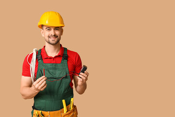 Portrait of male electrician with multimeter and wires on beige background