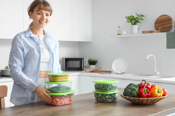 Young woman holding plastic containers with frozen vegetables in kitchen