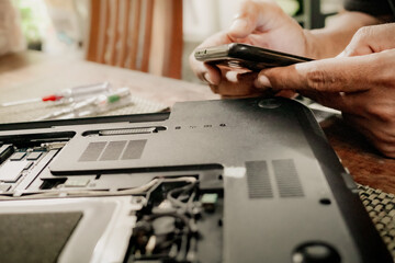 Male person searching for instructions from the internet using smartphone to repair a broken laptop...