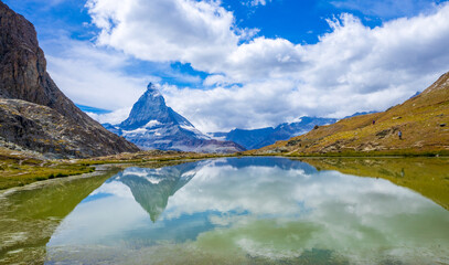 A view of the Matterhorn mountain peak in Switzerland reflected on a lake during a bright summer day.