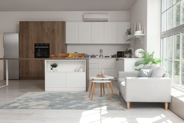 Modern interior of studio apartment with kitchen counter, stylish sofa and table near window