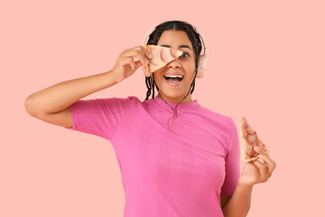 Young African-American woman in headphones with tasty pepperoni pizza on pink background