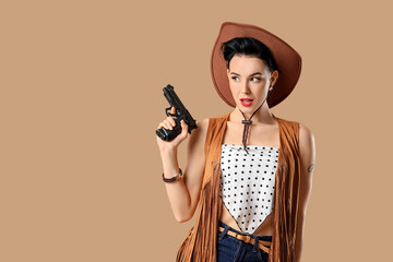 Young pin-up cowgirl with gun on brown background