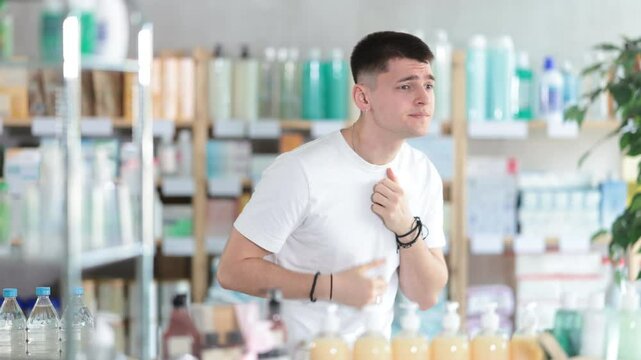European guy in a pharmacy with a sore throat and cough. Young man came to the pharmacy for medicines for colds and flu. Buyer in search of sore throat pills in a pharmacy. High quality 4k footage