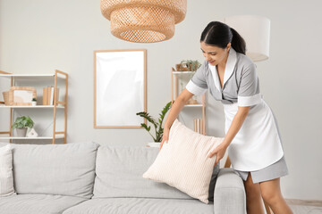 Young chambermaid putting pillow on sofa in hotel room