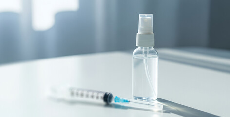 Clear disinfectant spray bottle and medical syringe placed on a white surface under soft daylight, reflecting sterilization tools used in clinical or home care settings.