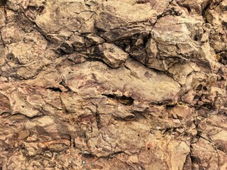 Rough textured surface of weathered brown rock with cracks