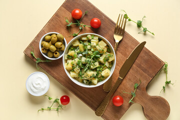 Bowl of tasty potato salad with micro green and olives on yellow background