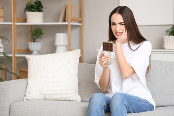 Young woman suffering from toothache with chocolate bar on sofa at home