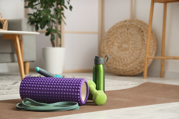 Sports equipment with foam roller, body massage roller, dumbbells and bottle of water on mat in...