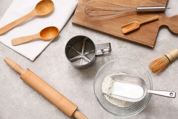 Set of different kitchen utensils with metal sieve mug and flour on grunge background