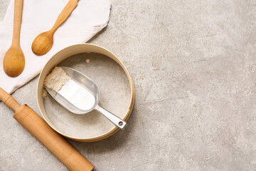 Metal scoop with flour in sieve, wooden spoons and rolling pin on grunge background