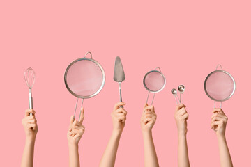 Female hands holding sieves with whisk, measuring spoons and cake spatula on pink background