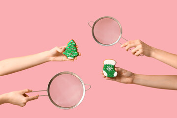 Female hands holding sieves with Christmas cookies on pink background