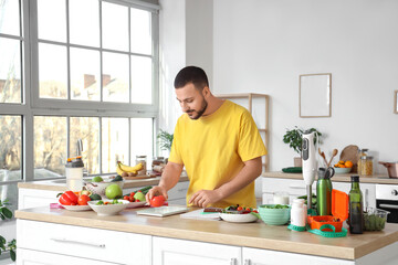 Handsome young man with fresh vegetables, scales and notebook planning his diet in kitchen. Healthy food concept