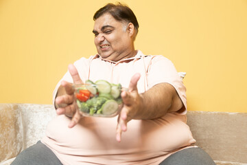 Unhappy overweight indian man avoid healthy salad food. Plus size guy refuse tasteless vegetable meal. Fat male say no to dieting. Obesity and weight loss concept.