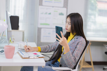 Young businesswoman sitting at a modern desk, comparing data from a computer and smartphone while...