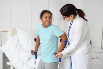 Teenage African-American girl with crutches and doctor walking in hospital room
