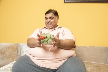 Unhappy overweight indian man avoid healthy salad food. Plus size guy refuse and feel disgusted to...