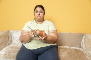 Plus size indian woman eating healthy vegetable salad food at home. Overweight fat female dieting to lose weight. Obesity concept.