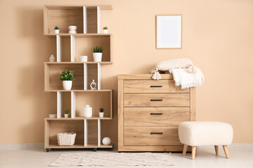 Interior of room with chest of drawers, pouf and shelving unit near beige wall