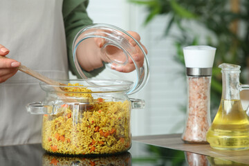 Woman preparing pilaf in cooking pot on stove, closeup