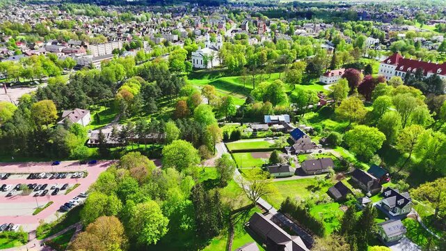 Vibrant green countryside with scattered houses transitions into a more densely packed city in the background, offering a contrast of rural and urban life from above.