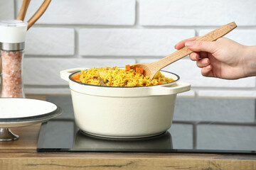 Woman preparing pilaf on stove in kitchen, closeup
