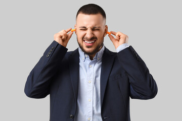 Young businessman suffering from loud noise on grey background
