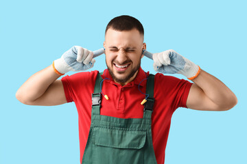 Male worker suffering from loud noise on blue background