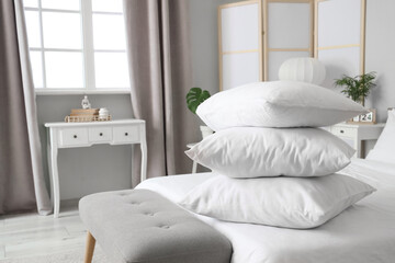 Comfortable bed with white blanket and stack of soft pillows in stylish bedroom, closeup