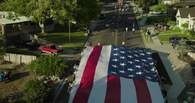 Majestic drone shot hovering over massive American flag being paraded down neighborhood street