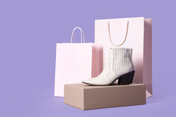 Shopping bags and leather boots on lilac background