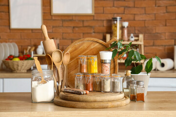 Jars with different spices, utensils and plant on table in kitchen
