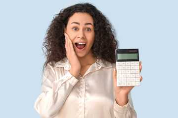 Happy African-American woman with calculator on light blue background