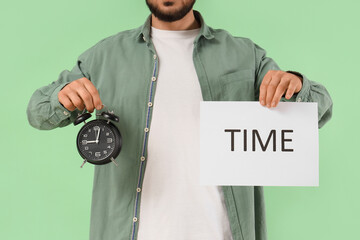 Man holding paper with word TIME and alarm clock on green background, closeup