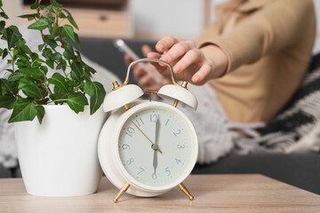 Woman with mobile phone and alarm clock on table at home, closeup