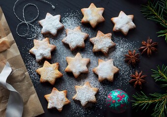 Star shaped baked gingerbread cookies sprinkled with powdered sugar on a black table, top view