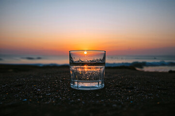 Refreshing glass of water against vibrant sunset beach