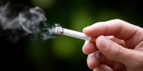Caucasian adult hand holding cigarette with smoke against green background