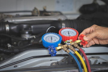 Auto mechanic using a gauge to check refrigerant and refill car air conditioning.
