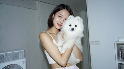 Young asian female holding fluffy white pomeranian dog indoors smiling
