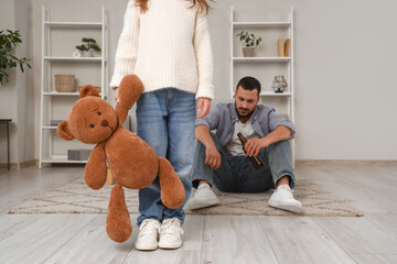 Sad girl with toy bear and her drunk father at home. Domestic violence concept